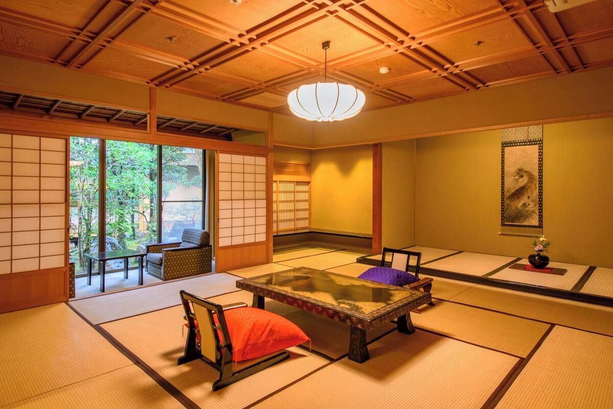 A traditional tatami room with tatami mats, a low table, cushions, sliding doors, and a hanging lantern.