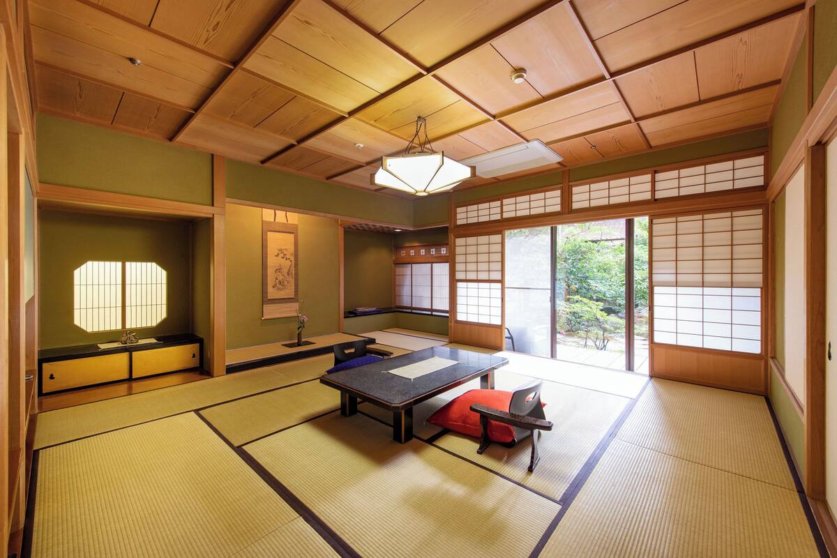 A tatami mat room with a low table, sliding doors, and a view of greenery outside.