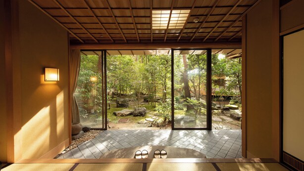 Una habitación japonesa tradicional con suelo de tatami, un puertas correderas de vidrio que dan a un jardín y un techo bajo con vigas de madera.