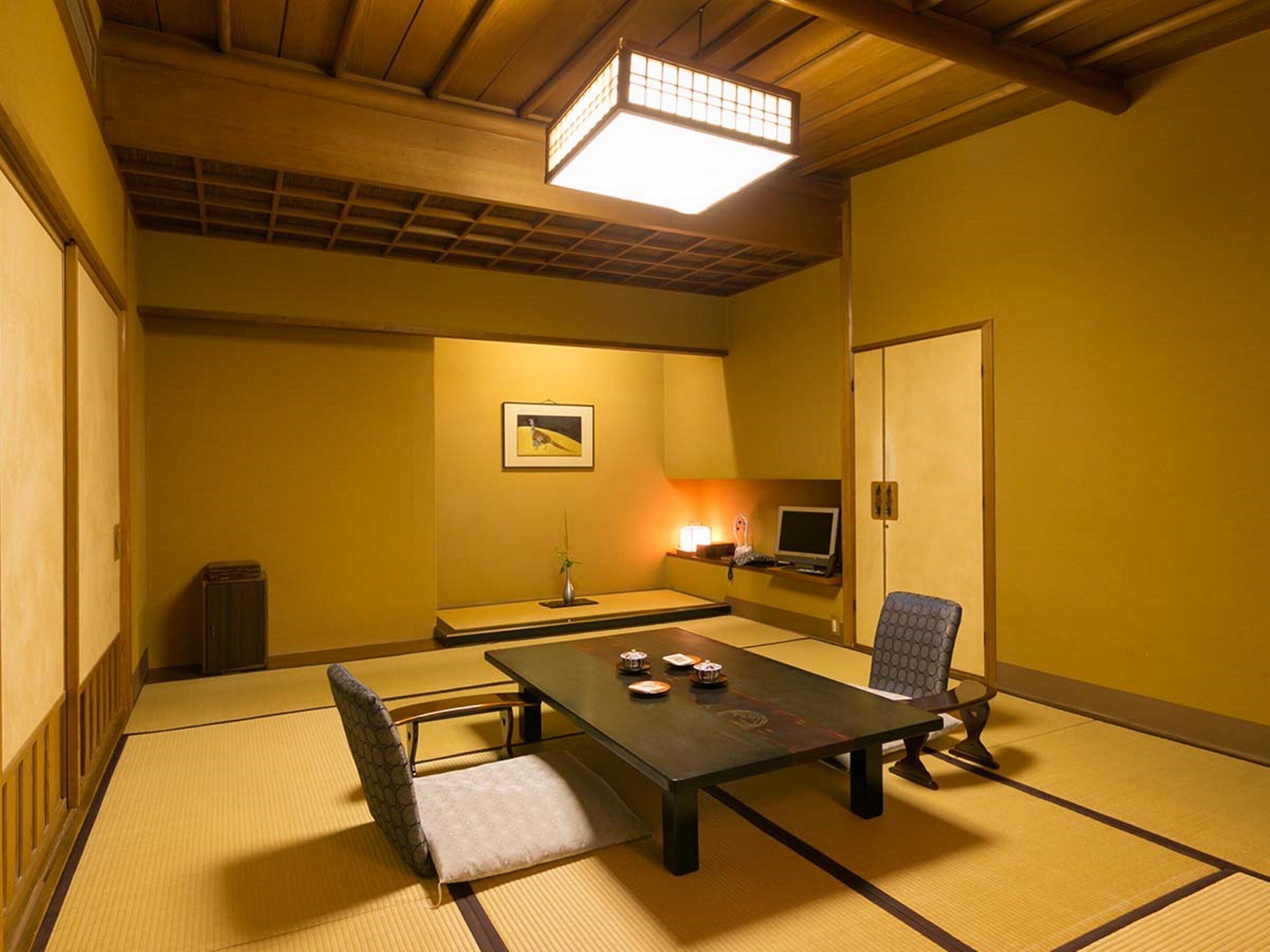 Une pièce de style japonais traditionnel, avec un sol recouvert de tatamis, une petite table avec un coussin, une chaise, un bureau avec un ordinateur et une lampe.