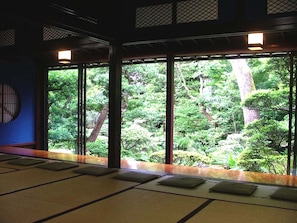 A traditional Japanese room with tatami mats, a view of a lush garden, and sliding doors. - Houshi (Komatsu)