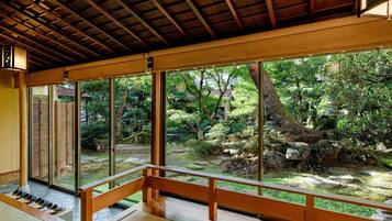 A traditional Japanese room with tatami flooring, a wooden bench, and a view of a garden through large sliding doors.