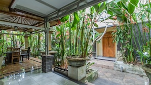 A covered patio with a tiled floor, surrounded by potted plants and a wooden door. - The Sesari Jimbaran (Jimbaran)