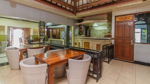 A dining area with a wooden table and wicker chairs, a kitchen area with a counter and cabinets, and a decorative ceiling with intricate designs. - The Sesari Jimbaran (Jimbaran)