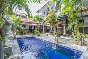 Una piscina rodeada de plantas tropicales y un edificio de dos pisos con balcones.