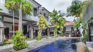 A swimming pool surrounded by lush greenery and a multi-story building with balconies. - The Sesari Jimbaran (Jimbaran)