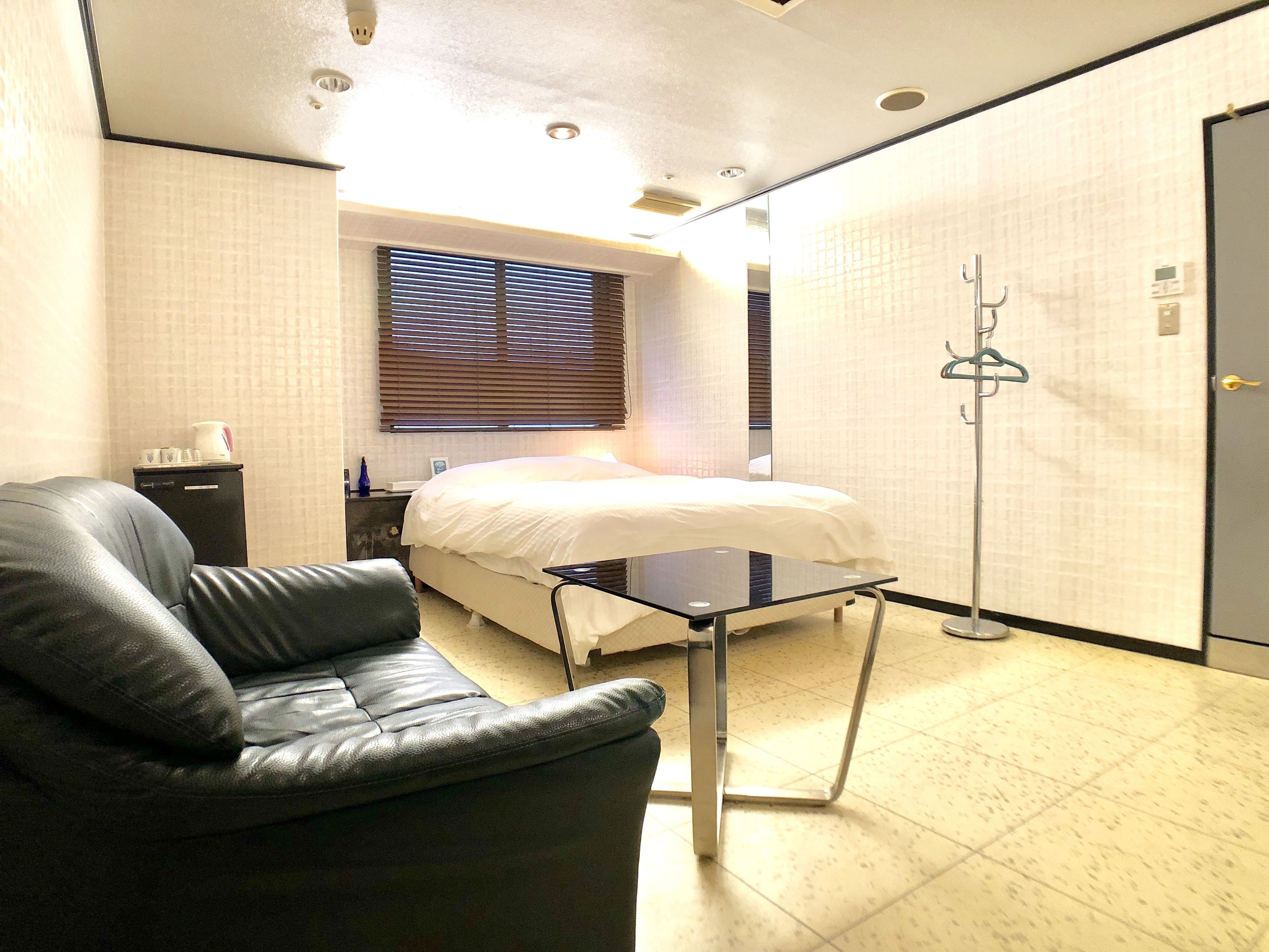 A hotel room with a bed, a chair, a small table, and a coat rack.