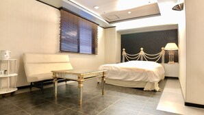 Une chambre d’hôtel moderne équipée d’un lit, d’une petite table, d’un canapé, d’une lampe et d’une fenêtre avec des stores.