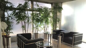 Un espace de détente moderne avec des canapés en cuir noir, une table basse en verre et de grandes plantes en pot.