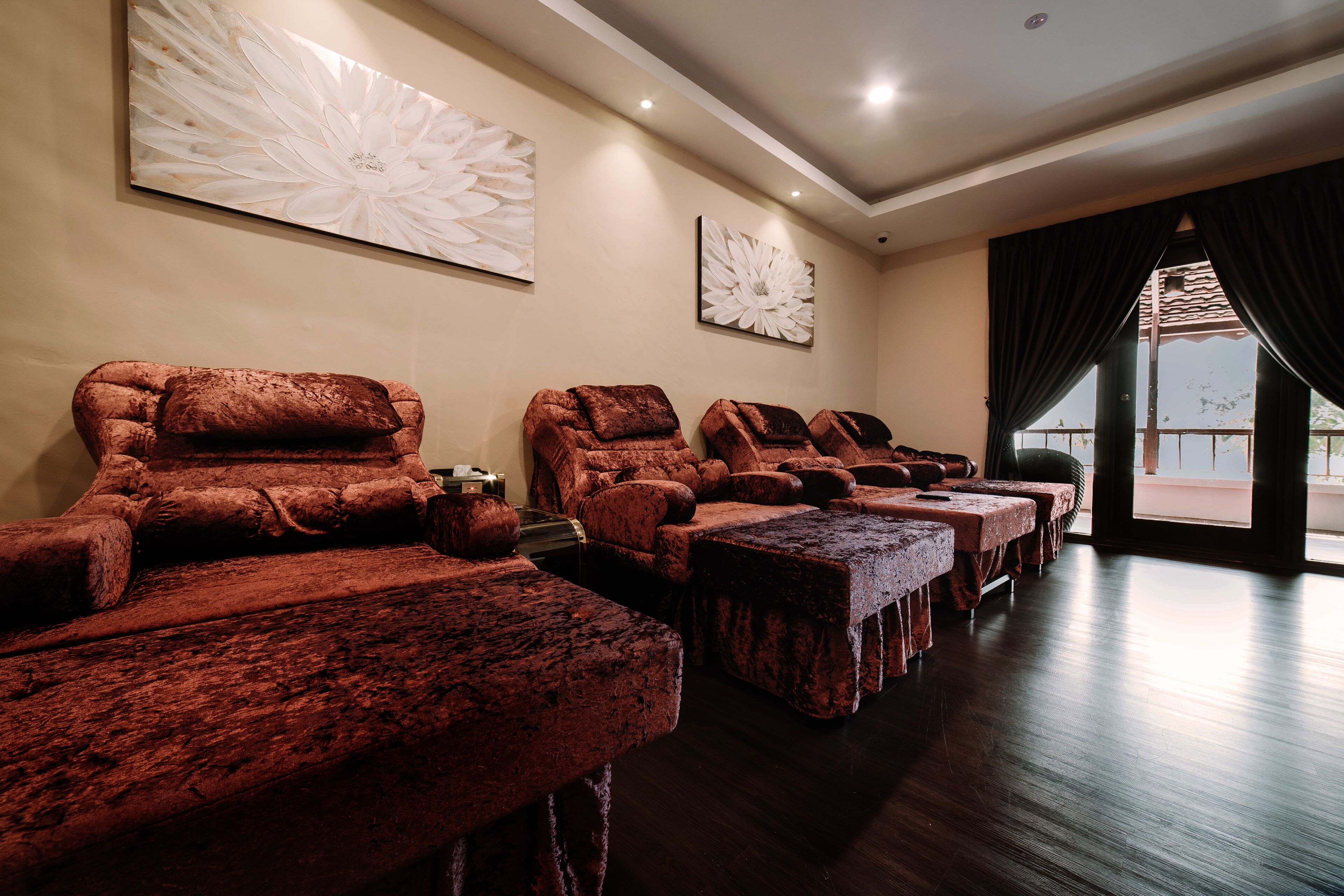 A room with multiple massage chairs and tables, a large window with curtains, and artwork on the walls.