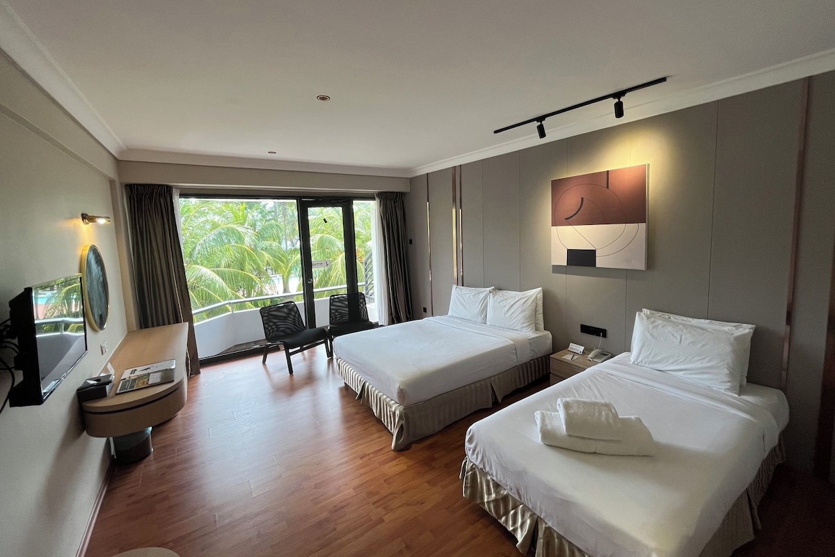 Une chambre d’hôtel avec deux lits, un bureau avec un ordinateur, une chaise et une grande fenêtre donnant sur des palmiers.