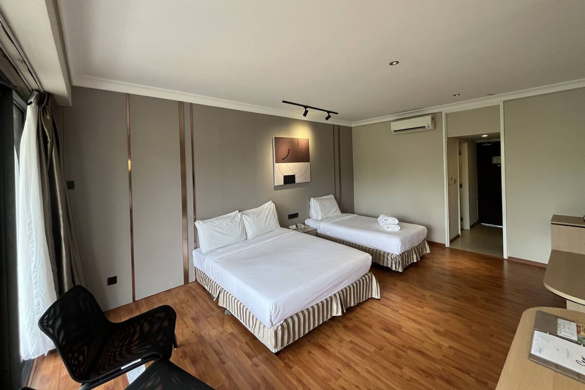 A hotel room with two beds, a desk, a chair, and a wall-mounted air conditioner.