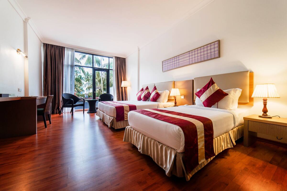 A hotel room with two beds, a desk, and a chair.