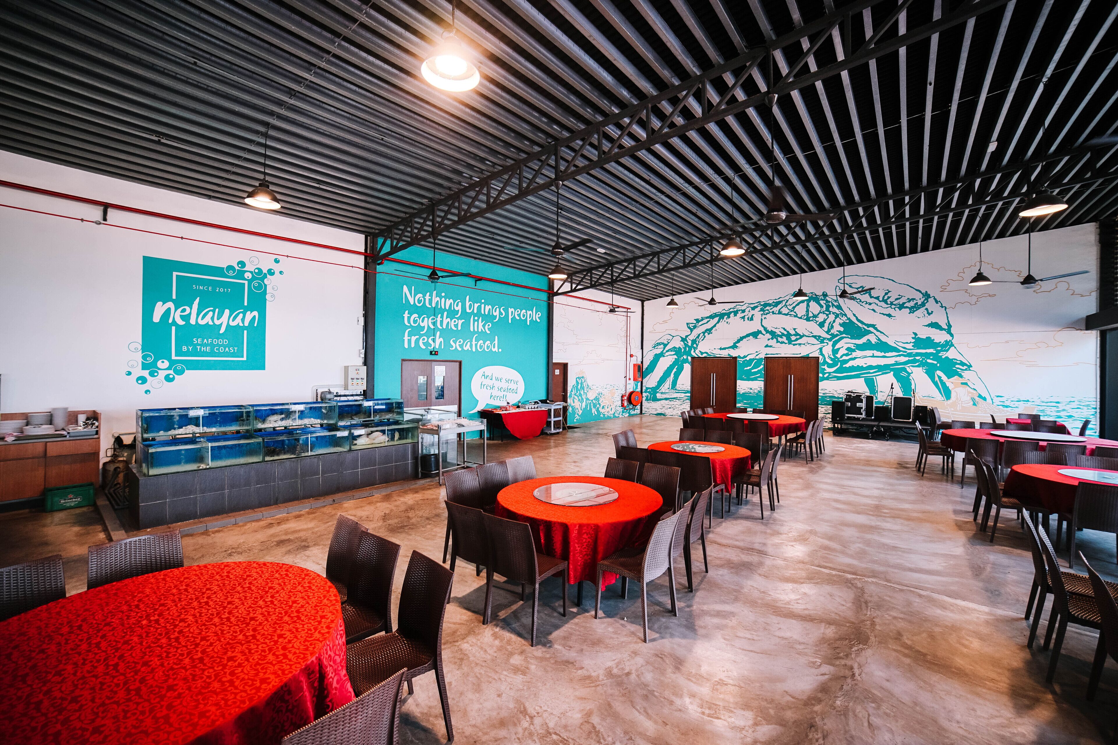 A restaurant interior with a seafood theme, featuring a large mural, red tables, and a modern industrial ceiling.