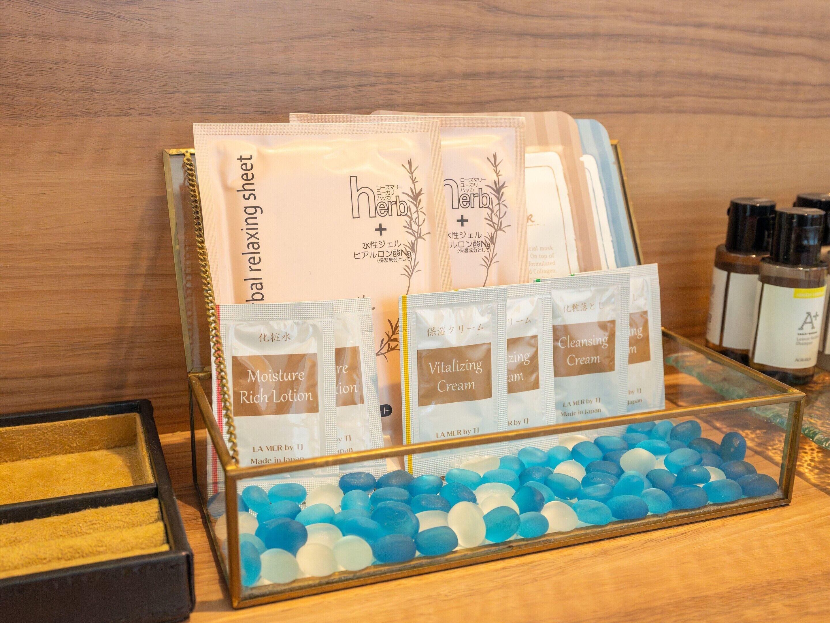 A display of skincare products including Moisture Rich Lotion, Vitalizing Cream, and Cleansing Cream, along with a glass container filled with blue and white stones.