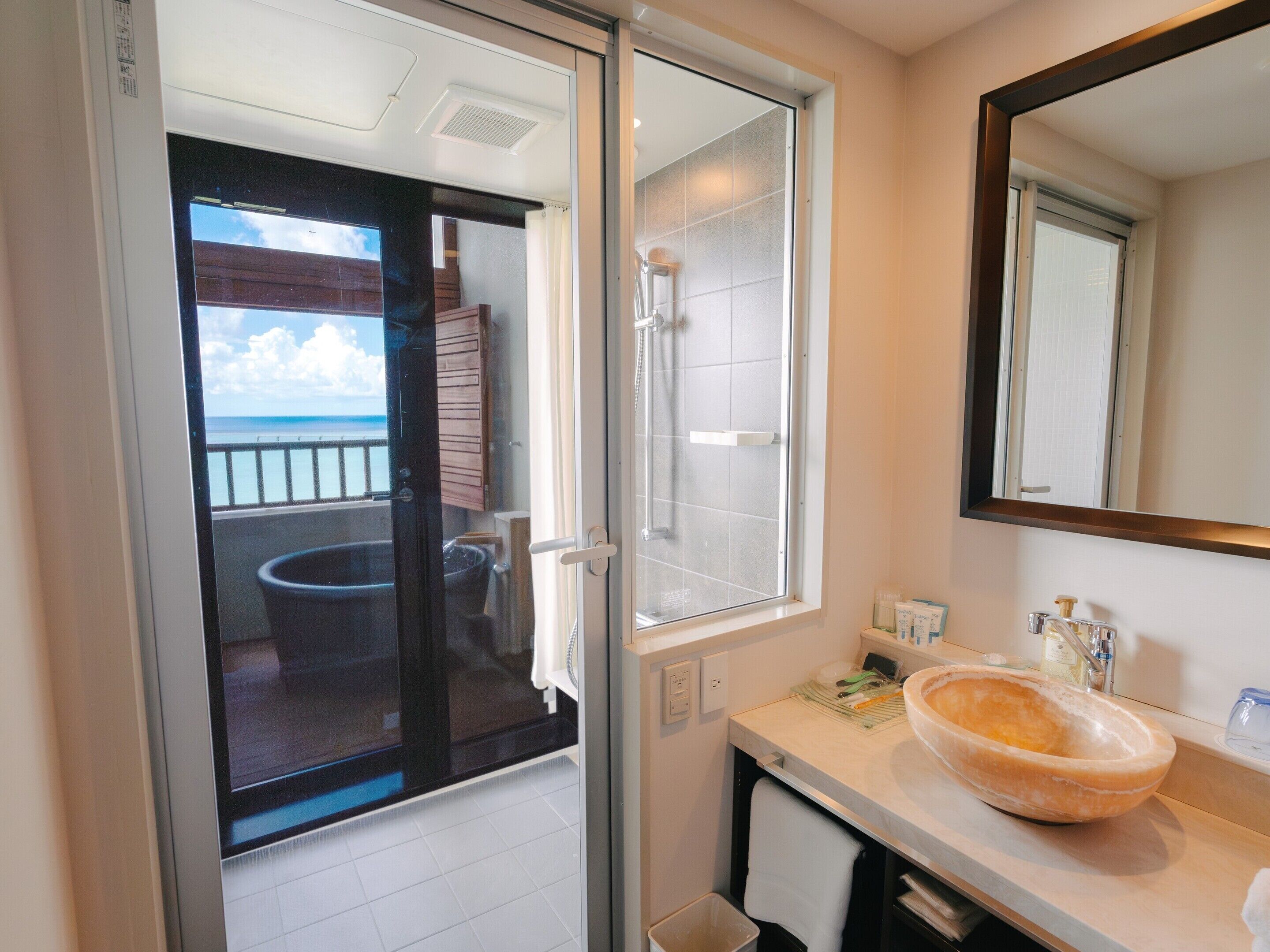 Ein Badezimmer mit Glastür, die auf einen Balkon führt, einem großen Spiegel und einem Waschbecken.