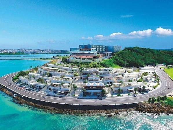 Un resort costero con una carretera circular, villas frente a la playa y un edificio moderno.
