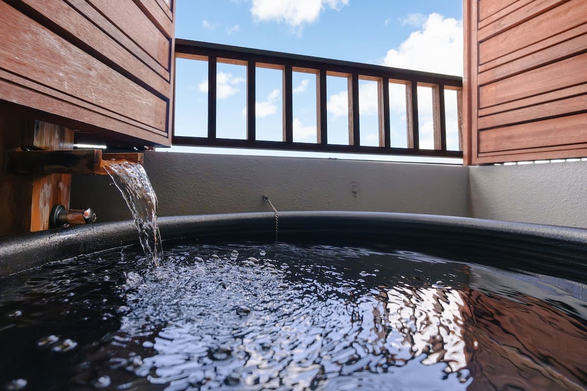 A hot tub with water flowing into it, surrounded by wooden panels and a clear sky.