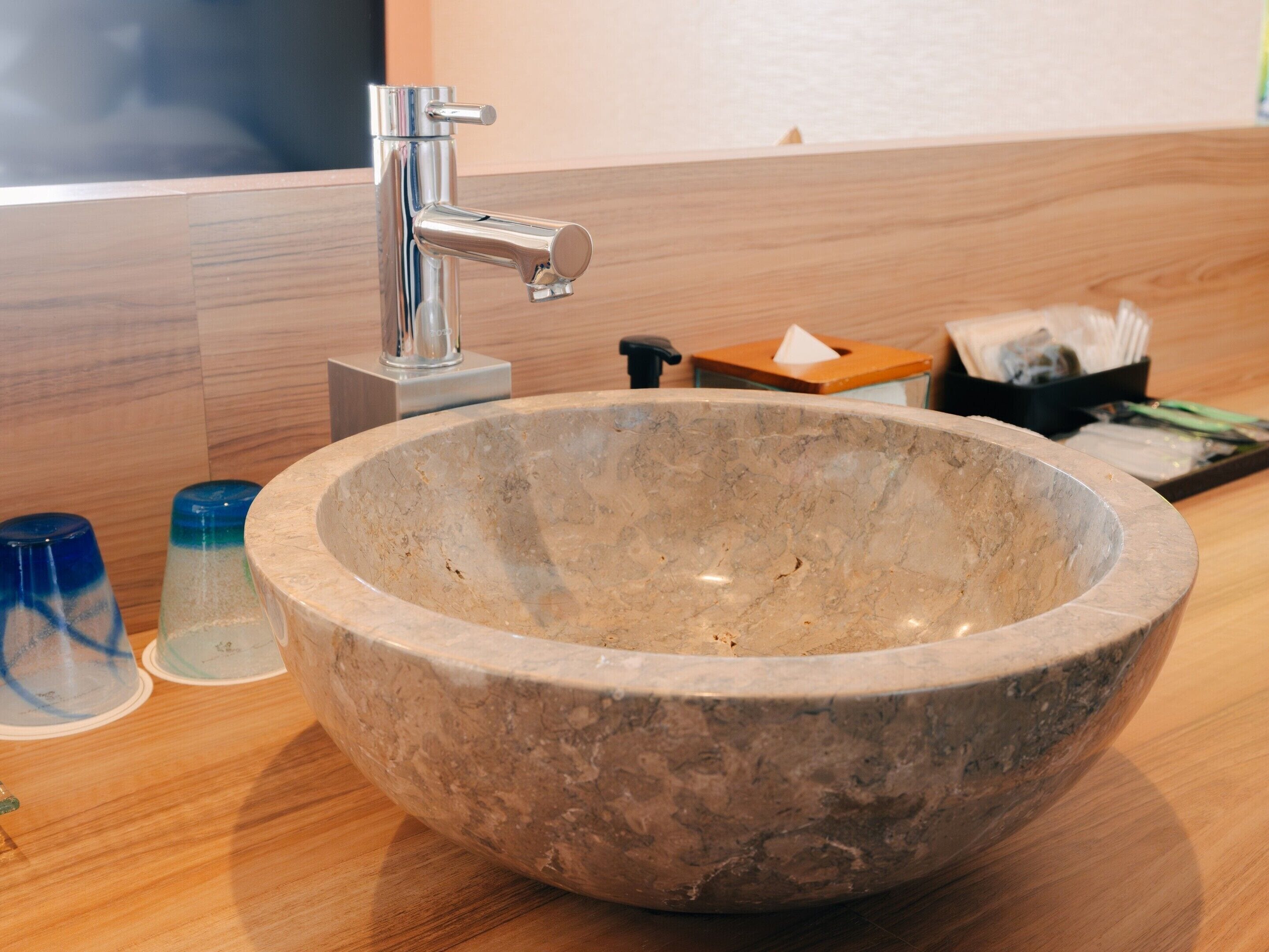 Un baño con lavamanos de mármol, un grifo moderno y una encimera de madera.