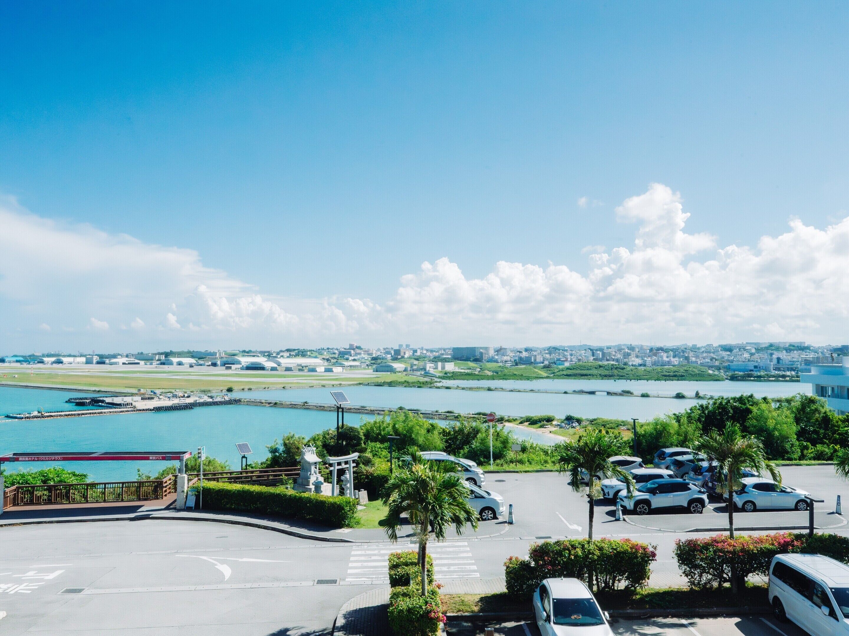 A parking area with cars, a pedestrian crossing, and a view of a cityscape and water body.