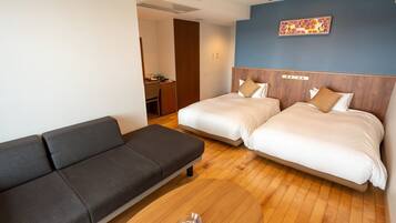A hotel room with two beds, a sofa, a wooden floor, and a wall-mounted artwork.