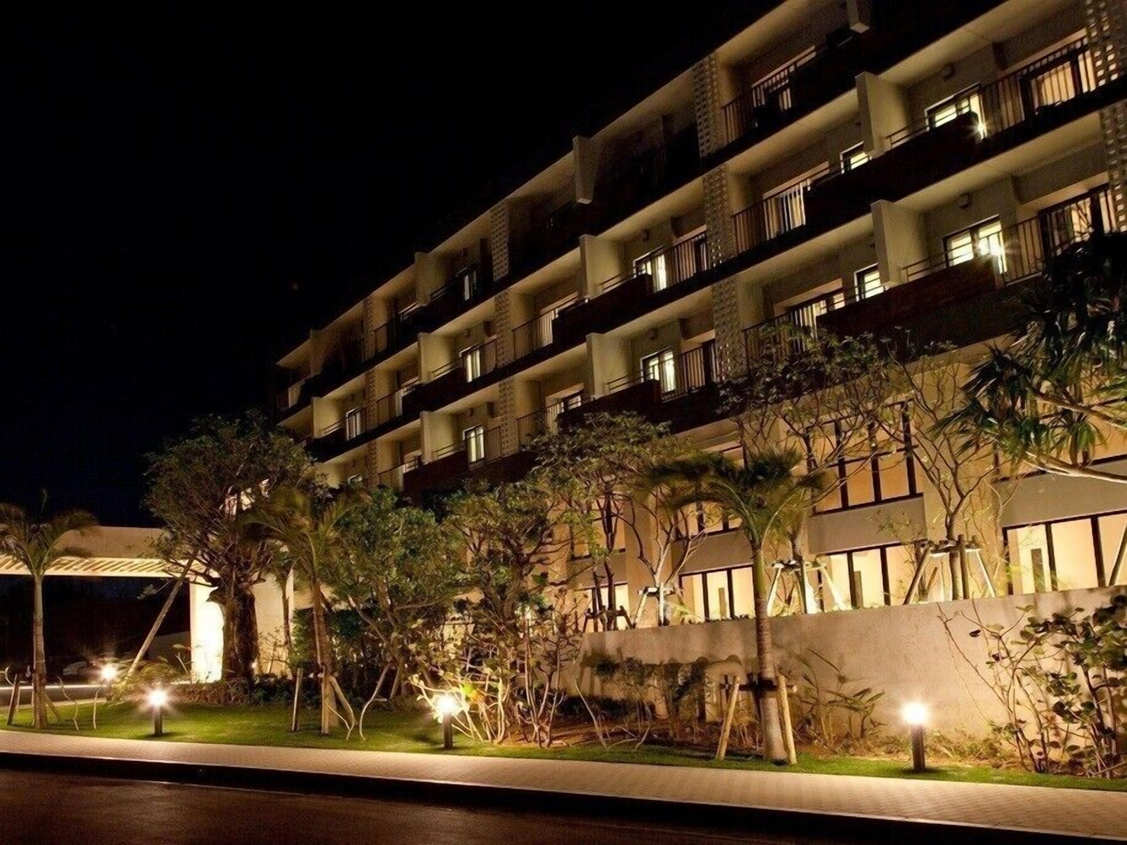 A multi-story hotel with balconies, a well-lit entrance, and a landscaped garden area.