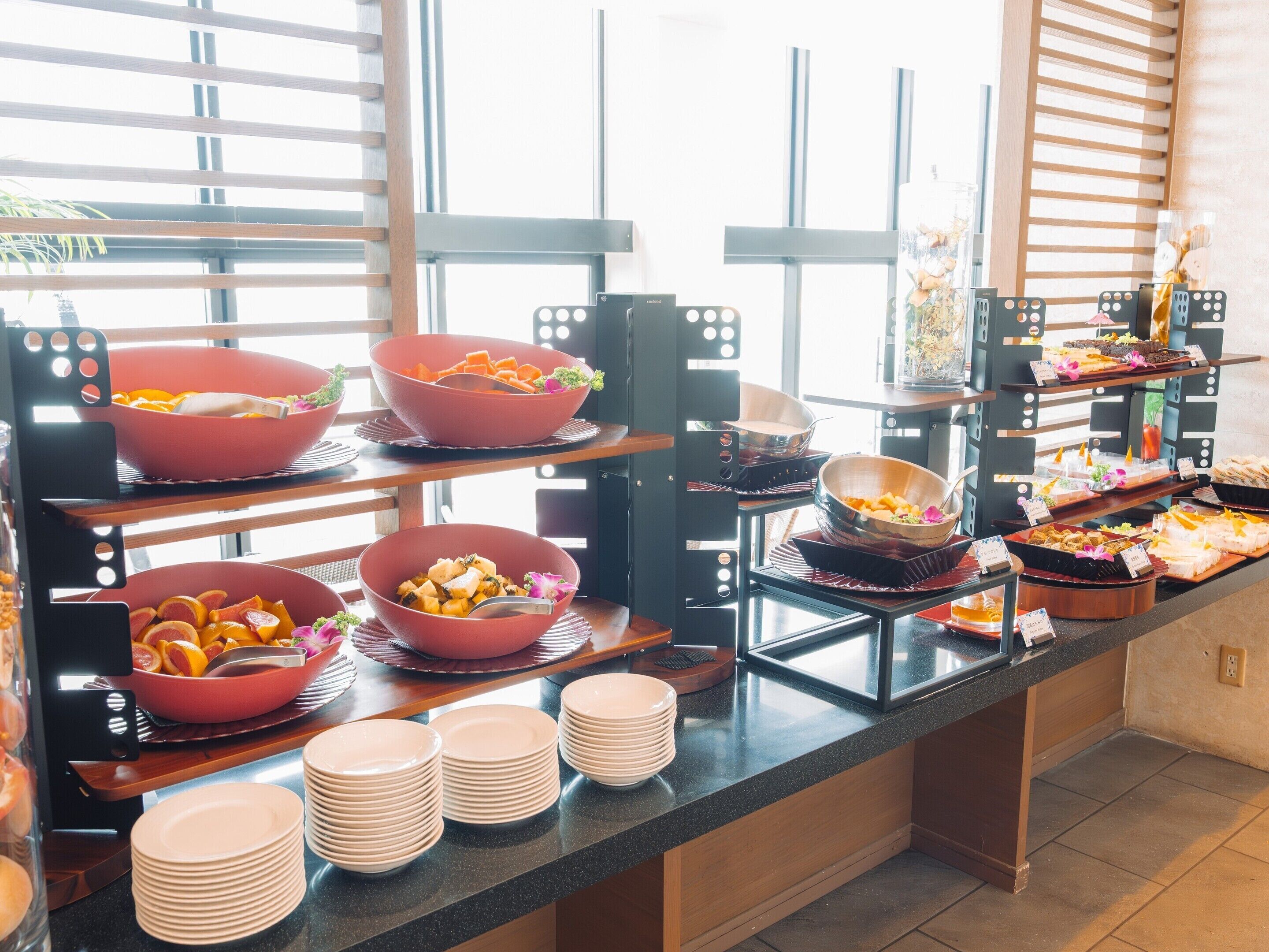 Disposição de buffet com diversos alimentos e recipientes em prateleiras.