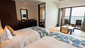 A hotel room with two beds, a desk, a chair, and a balcony with a view.