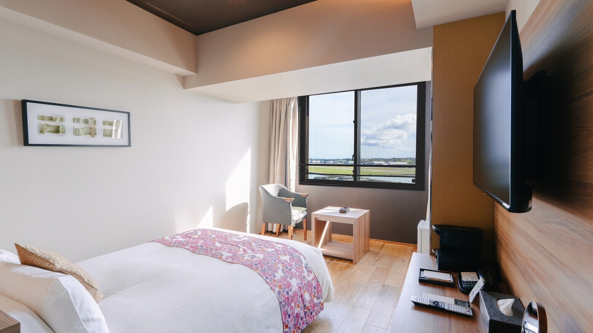 A hotel room with a bed, a desk, a chair, a television, and a window with a view.