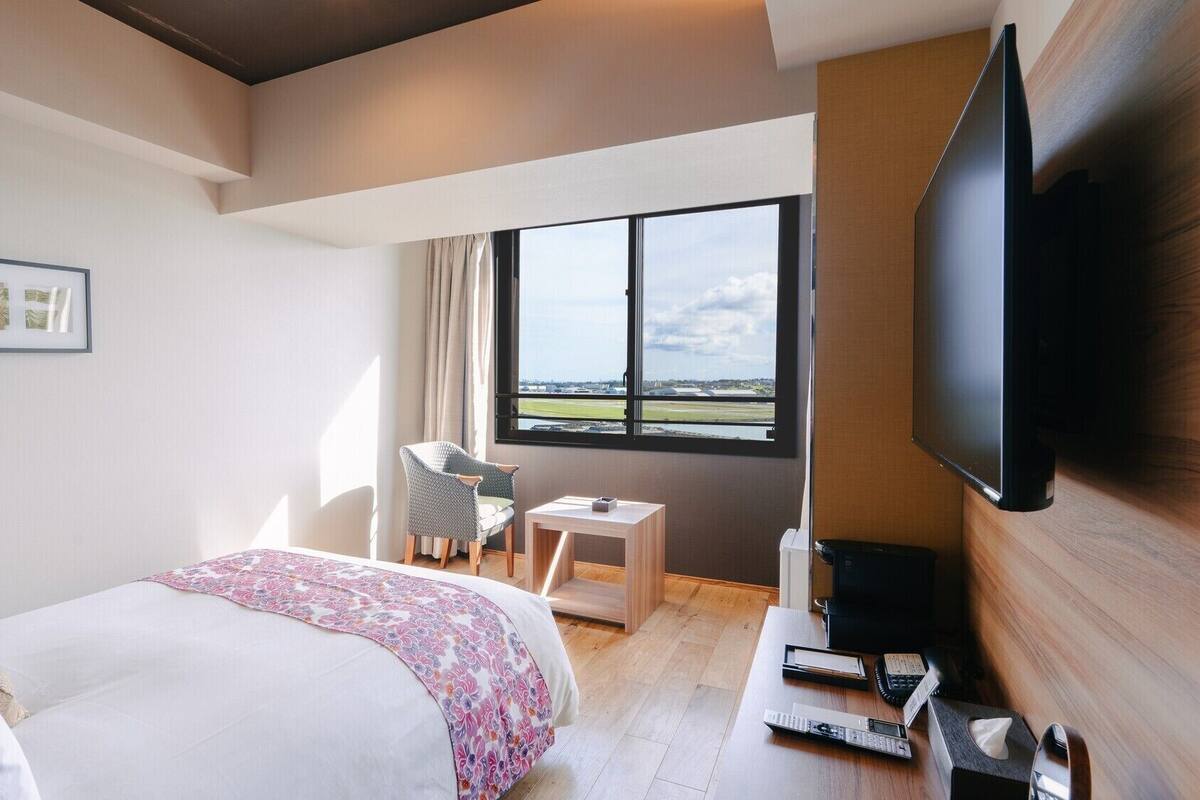 A hotel room with a bed, a desk, a chair, a television, and a window with a view.