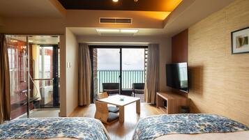 Habitación de hotel con dos camas, televisor, balcón con vistas y una mesa con sillas.