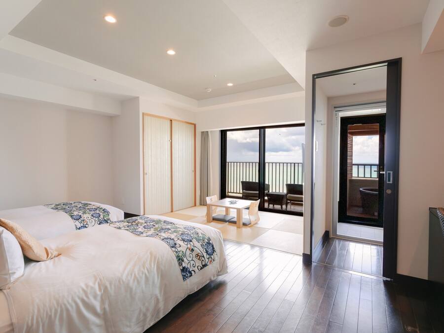 Una habitación de hotel con una cama grande, un balcón con mesa y sillas, y vistas al mar.