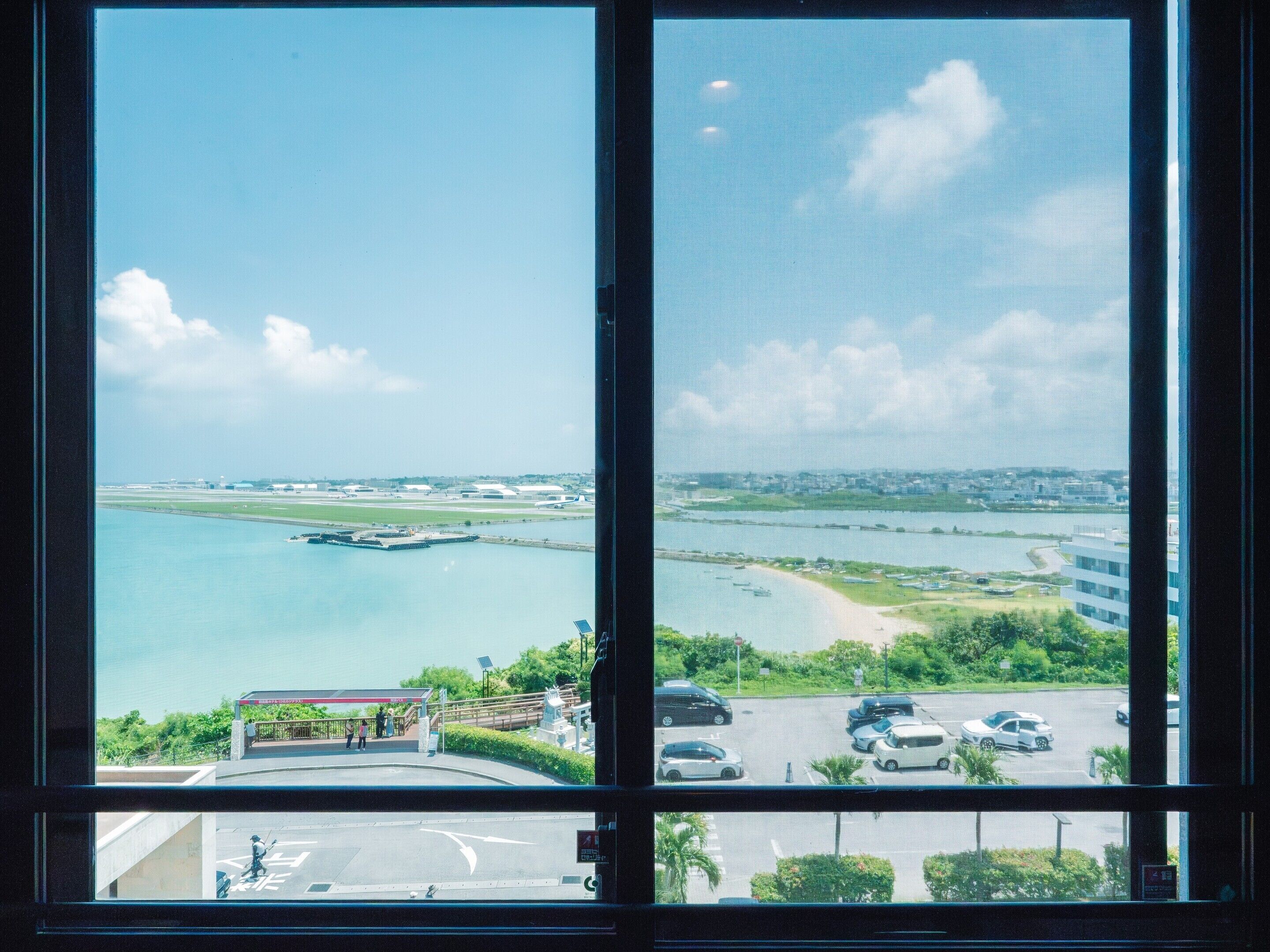 A view through a window of a coastal area with a marina, a bridge, and a parking lot.