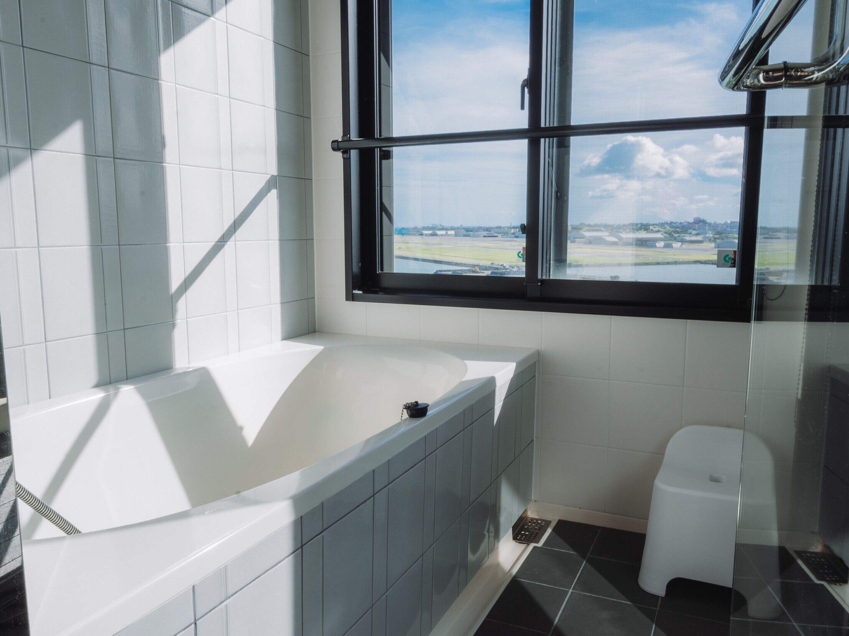 A modern bathroom with a bathtub, a window with a view of a landscape, and a white toilet.