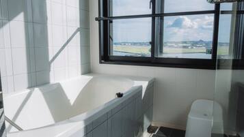 A modern bathroom with a bathtub, a window with a view of a landscape, and a white toilet.