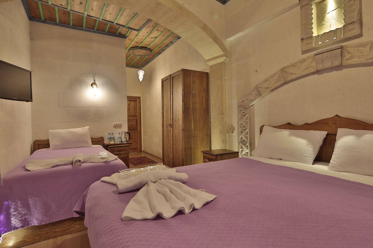 A hotel room with two beds, wooden headboards, a stone wall, and a wooden ceiling.