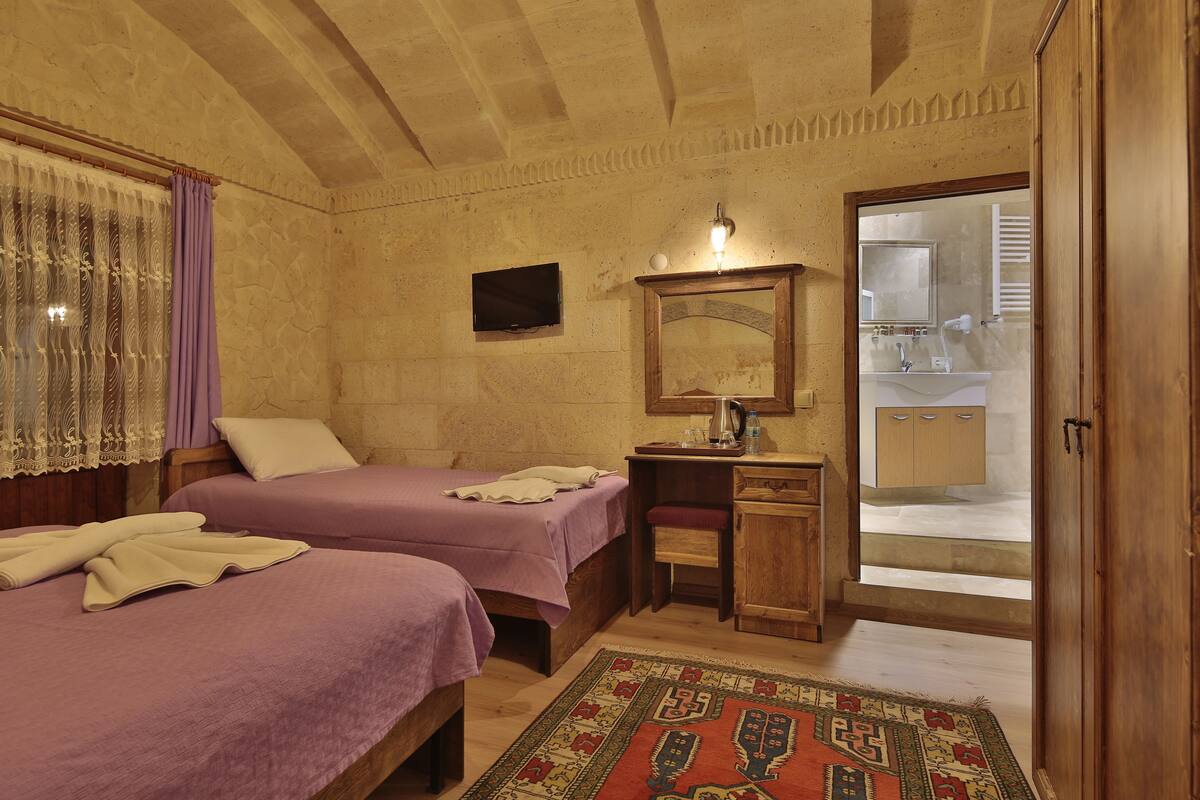 A room with two beds, a desk, a mirror, and a bathroom visible through an open door.