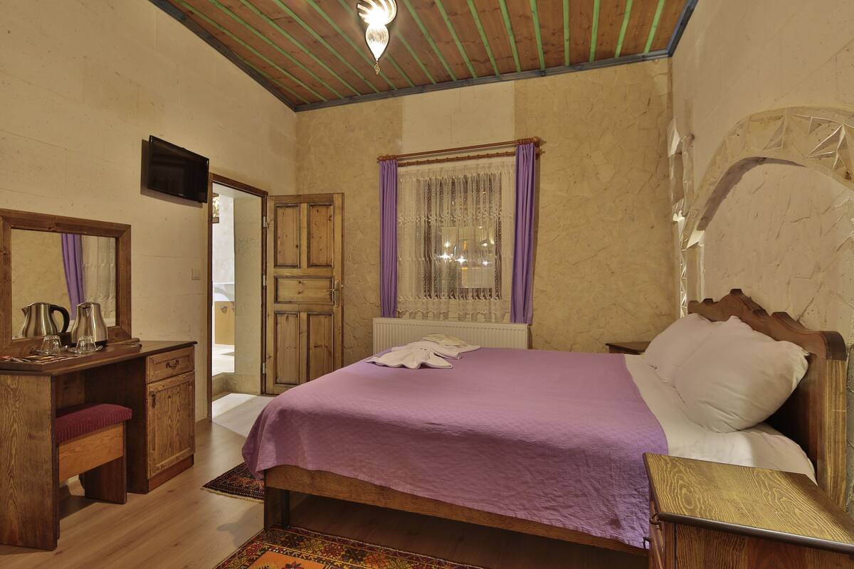 A bedroom with a wooden bed, a desk with a mirror, a radiator, and a window with purple curtains.