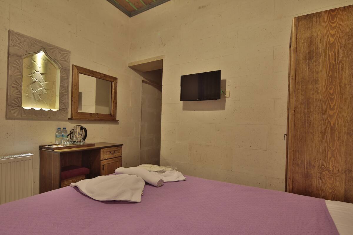 A bedroom with a bed, a wooden dresser, a mirror, a television, and a wooden door.