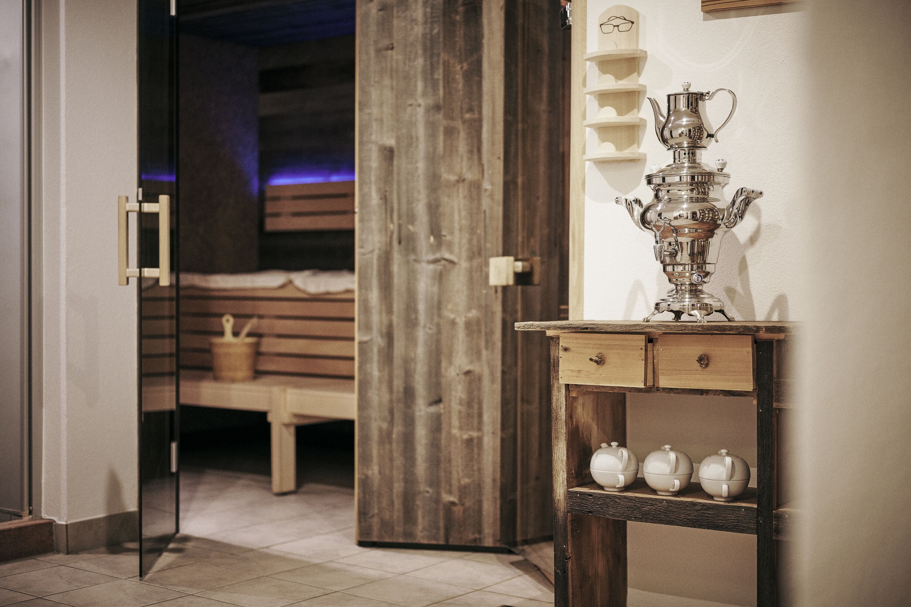 A wooden door leading to a room with a bench and a shelf with teapots.