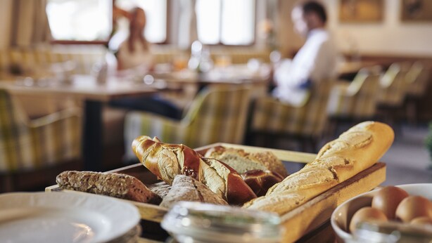A dining area with tables and chairs, a variety of bread on a tray, and a bowl of eggs. - Der Klostertalerhof (Klösterle am Arlberg)