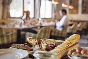 A dining area with tables and chairs, a variety of bread on a tray, and a bowl of eggs. - Der Klostertalerhof (Klösterle am Arlberg)