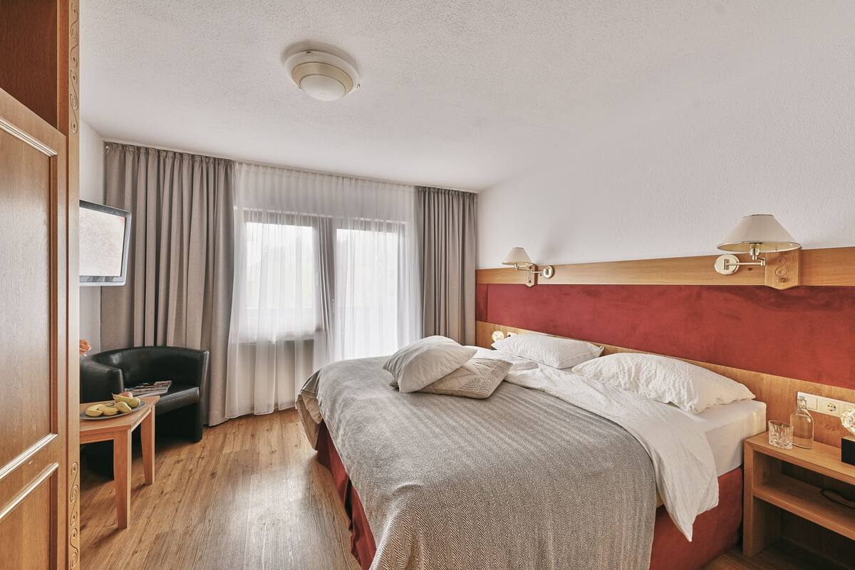 A hotel room with a bed, a desk, a chair, and a window with curtains.