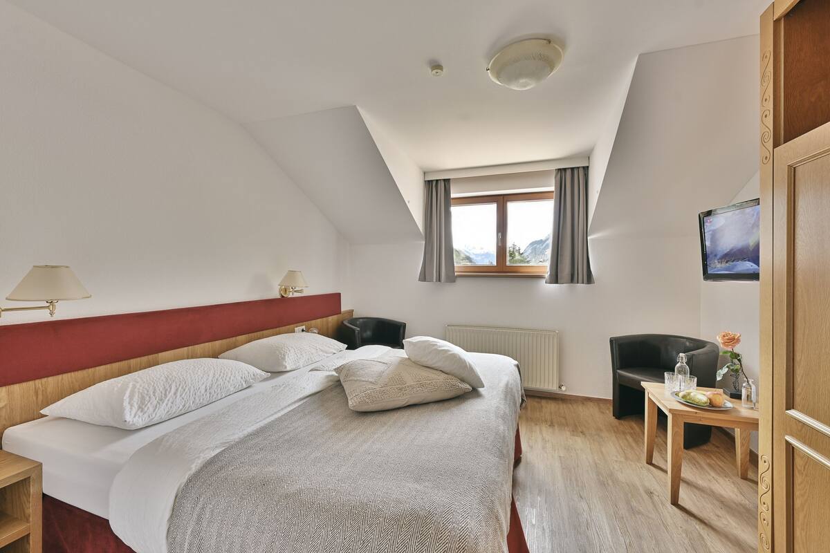 A hotel room with a bed, a desk, a chair, a TV, and a window with curtains.