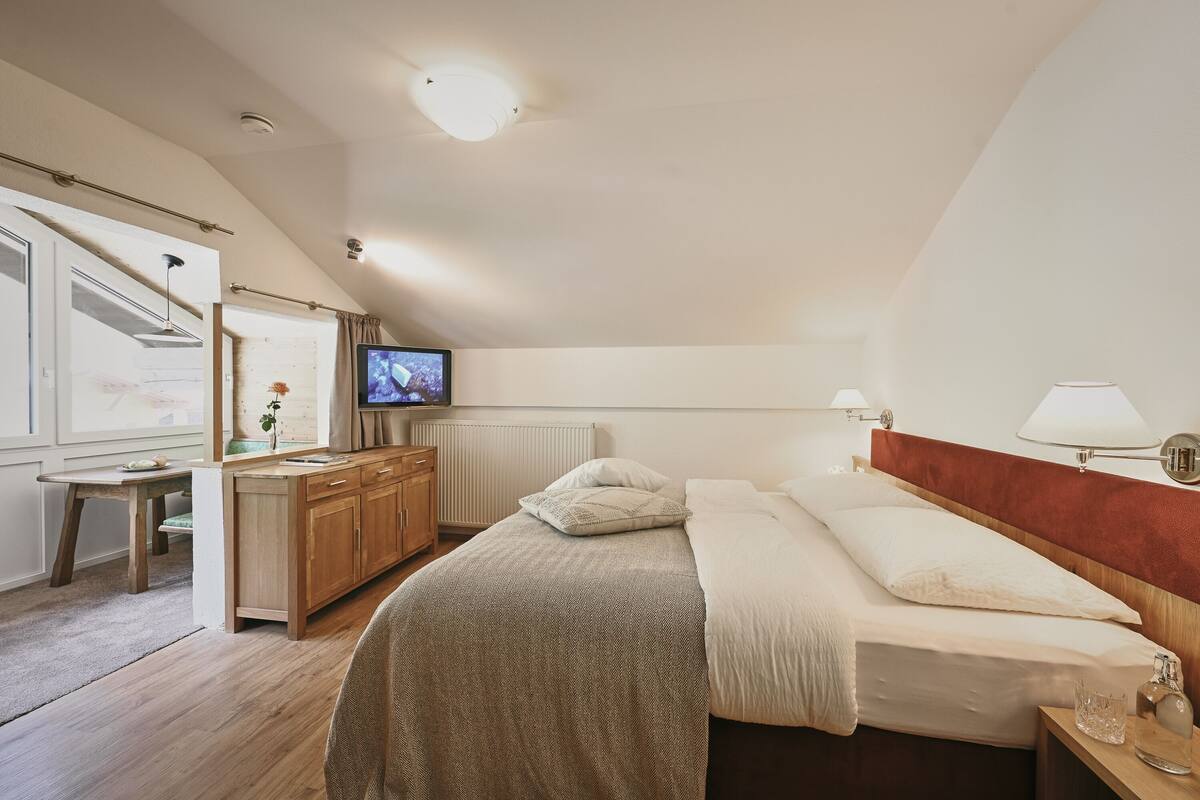A bedroom with a bed, bedside table, lamp, and a TV on a dresser.