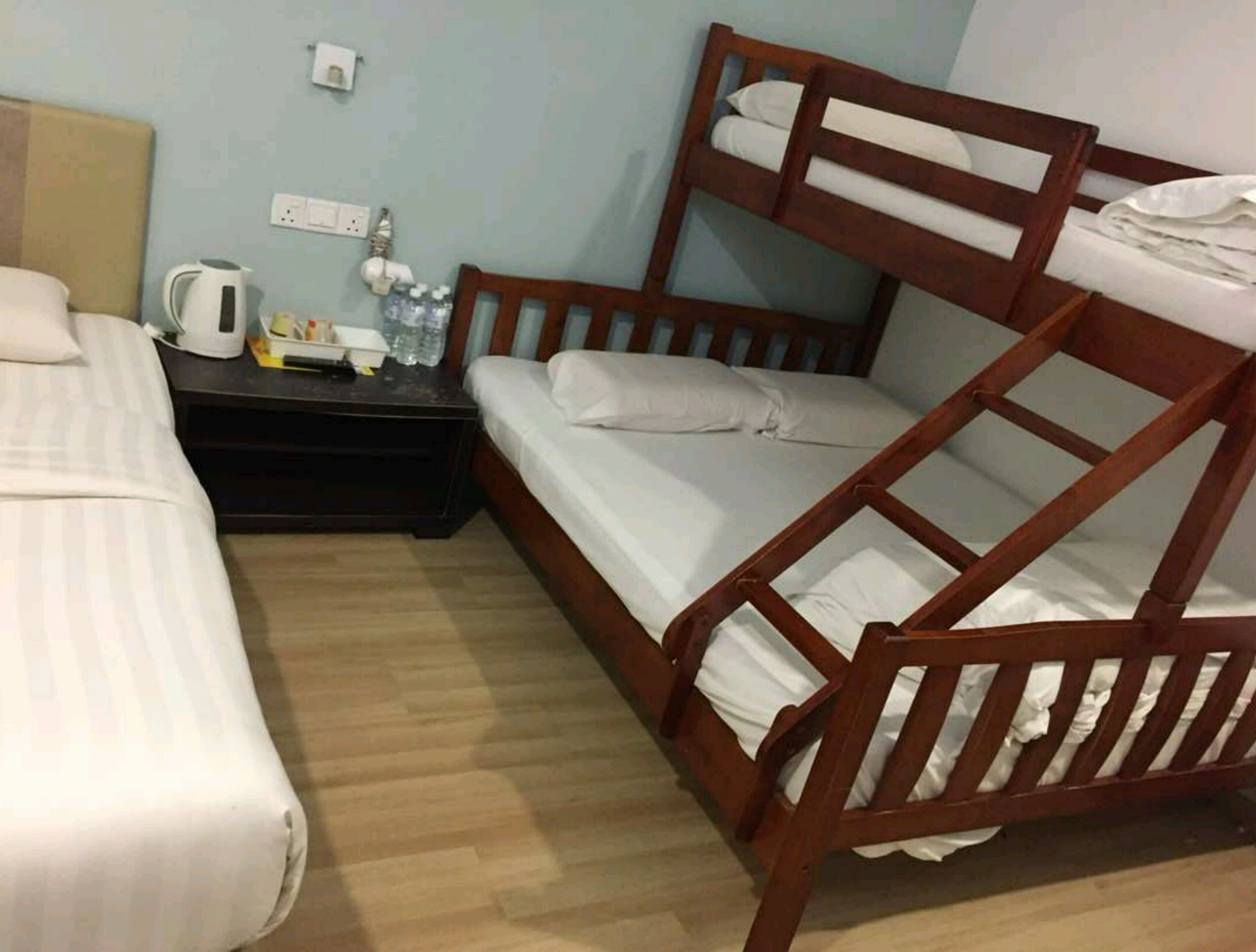 Ein Zimmer mit zwei Etagenbetten, einem Nachttisch mit Wasserkocher und einer Wasserflasche sowie einer Steckdose an der Wand.