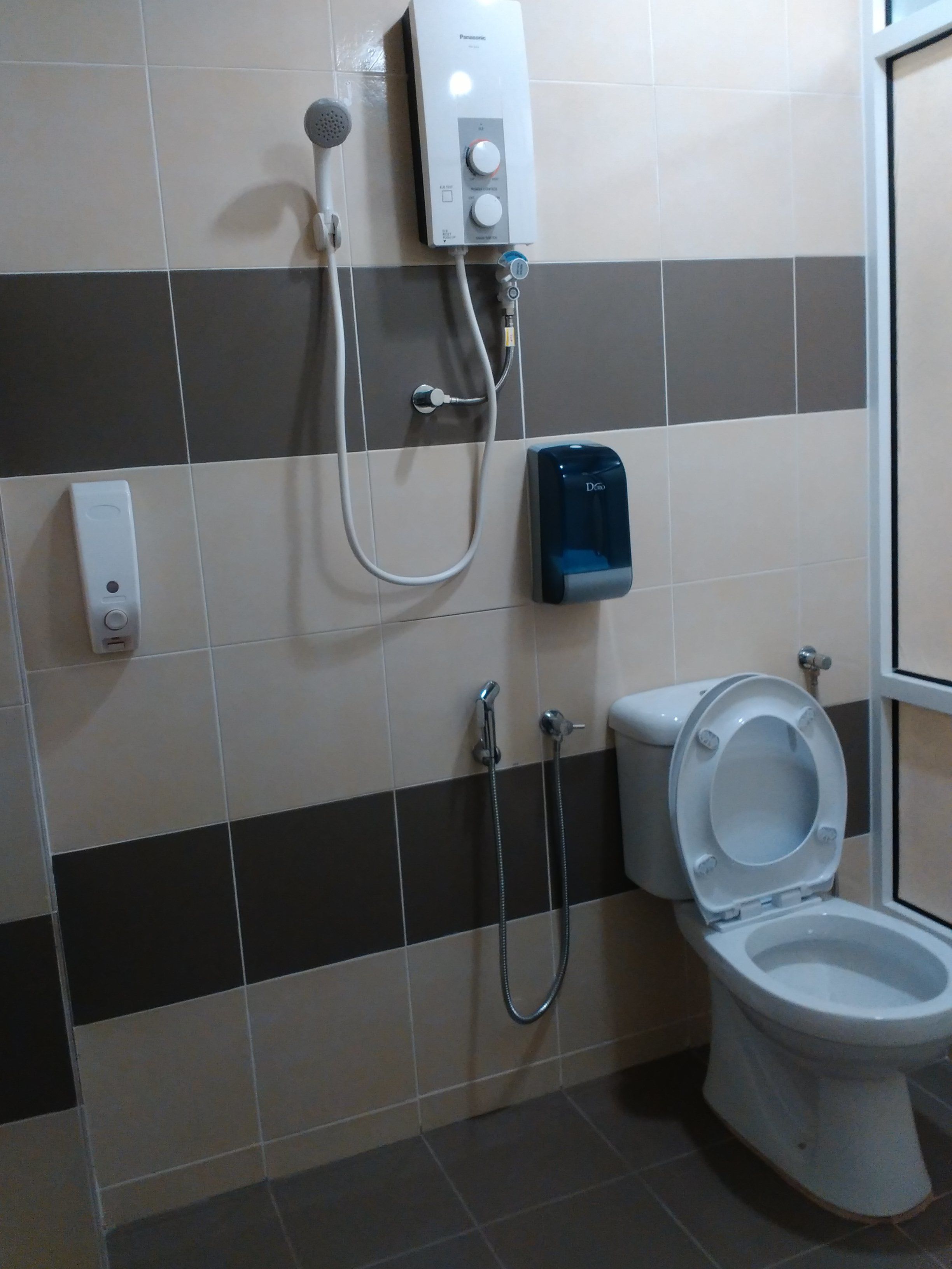 Un baño con inodoro, ducha y dispensador de jabón.