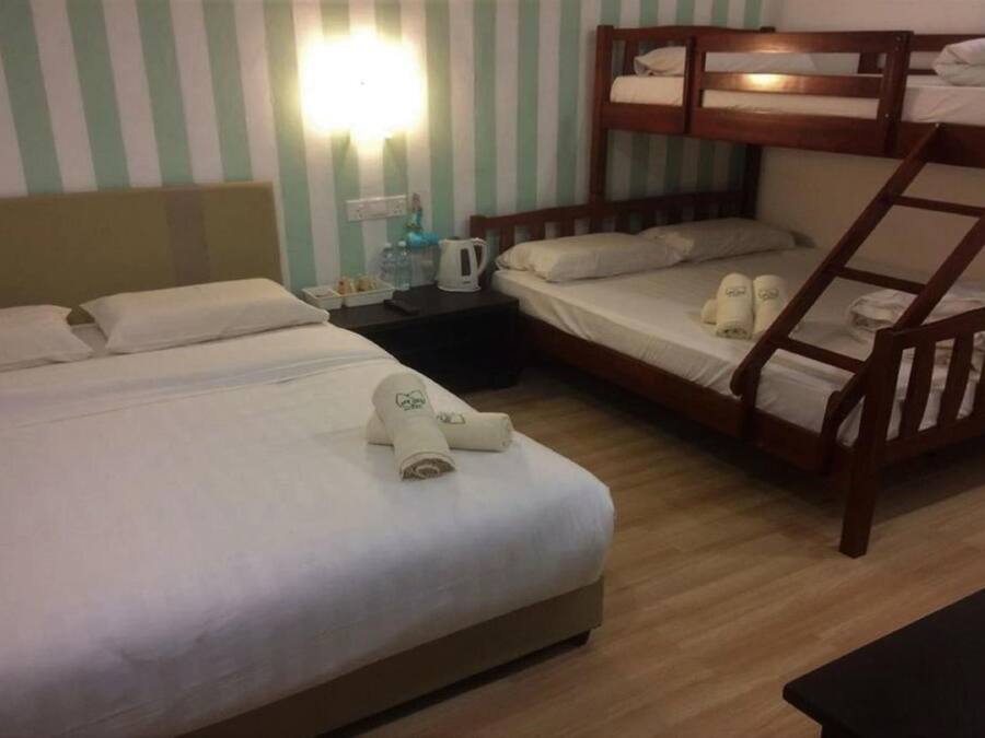 Habitación de hotel con dos camas, una litera de madera, una mesita de noche con hervidor y una lámpara fijada en la pared.