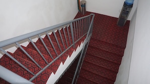 Una escalera con barandilla de metal, alfombra estampada, un dispensador de agua y un bote de basura.