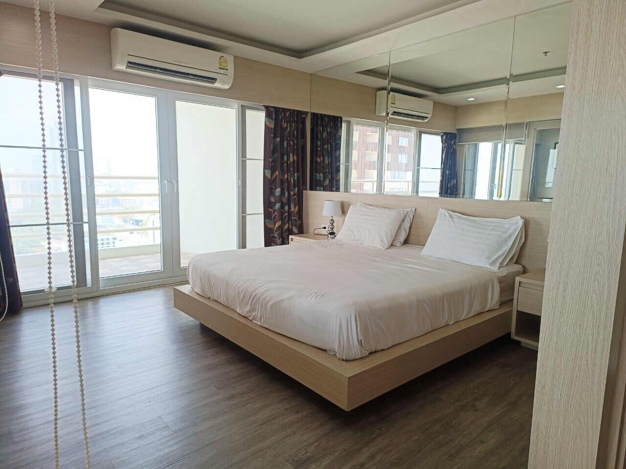 A modern hotel room with a large bed, a bedside table, a nightstand, and a window with curtains.